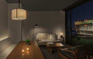 A dining area and seating area in a lamp-lit guest suite with a floor-to-ceiling window