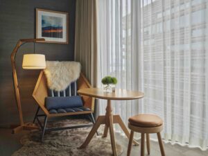 An armchair and side table next to a floor-to-ceiling window with light-filtering drapes