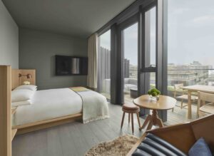 A queen bed and side table in a guest room with floor-to-ceiling windows