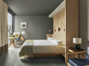 A guest room with a queen bed, adjustable reading lamps, an armchair and side table, and floor-to-ceiling window