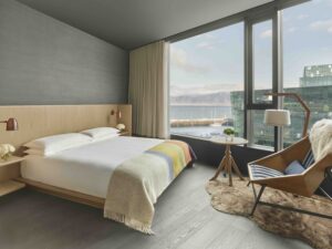 Guest room with a queen bed, an armchair and side table, and a floor-to-ceiling window